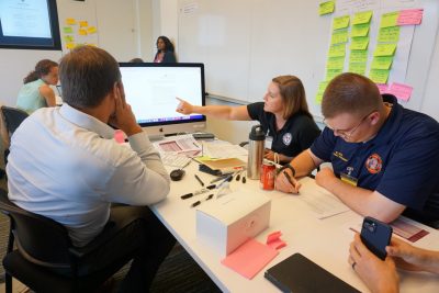 Three men and women sit at table during a discussion about artificial intelligence. One points to a computer screen with information displayed on it.