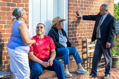 Four people talk while sitting and standing on the steps of a brick building.