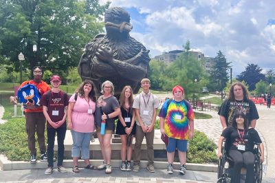 A group of teens and adults stand in front of a giant statue of the Virginia Tech HokieBird.