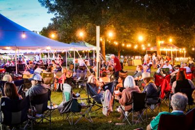 patrons enjoy the music while seated outside a large white tent at twilight