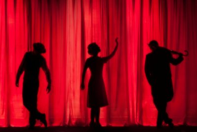 Three shadows of stage performers behind a red curtain.