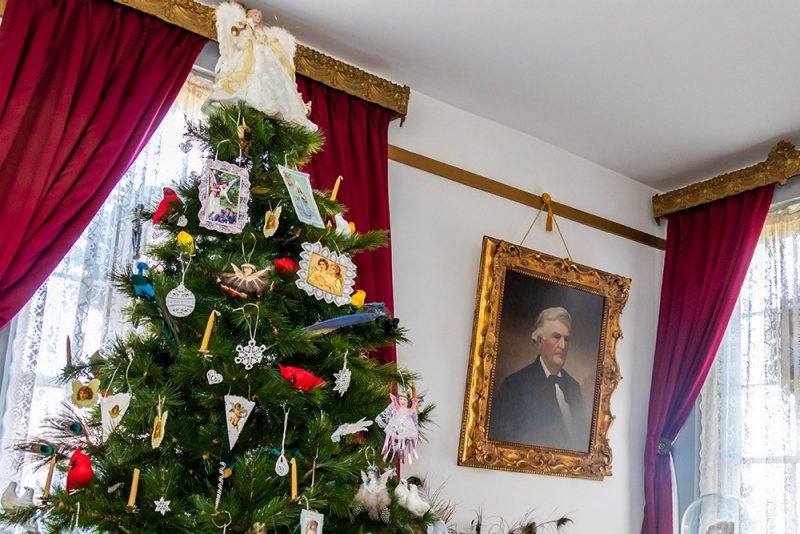 A Christmas tree with candles and hand-made ornaments is displayed next to an oil portrait of Harden Reynolds.